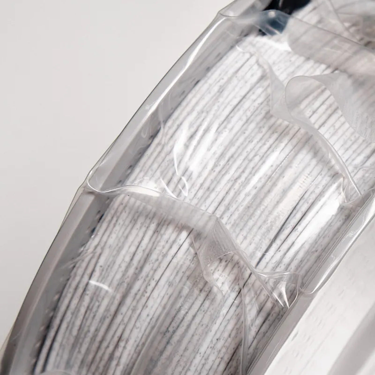 Close-up White Marble PLA filament windings with dark speckles, vacuum-sealed on white spool