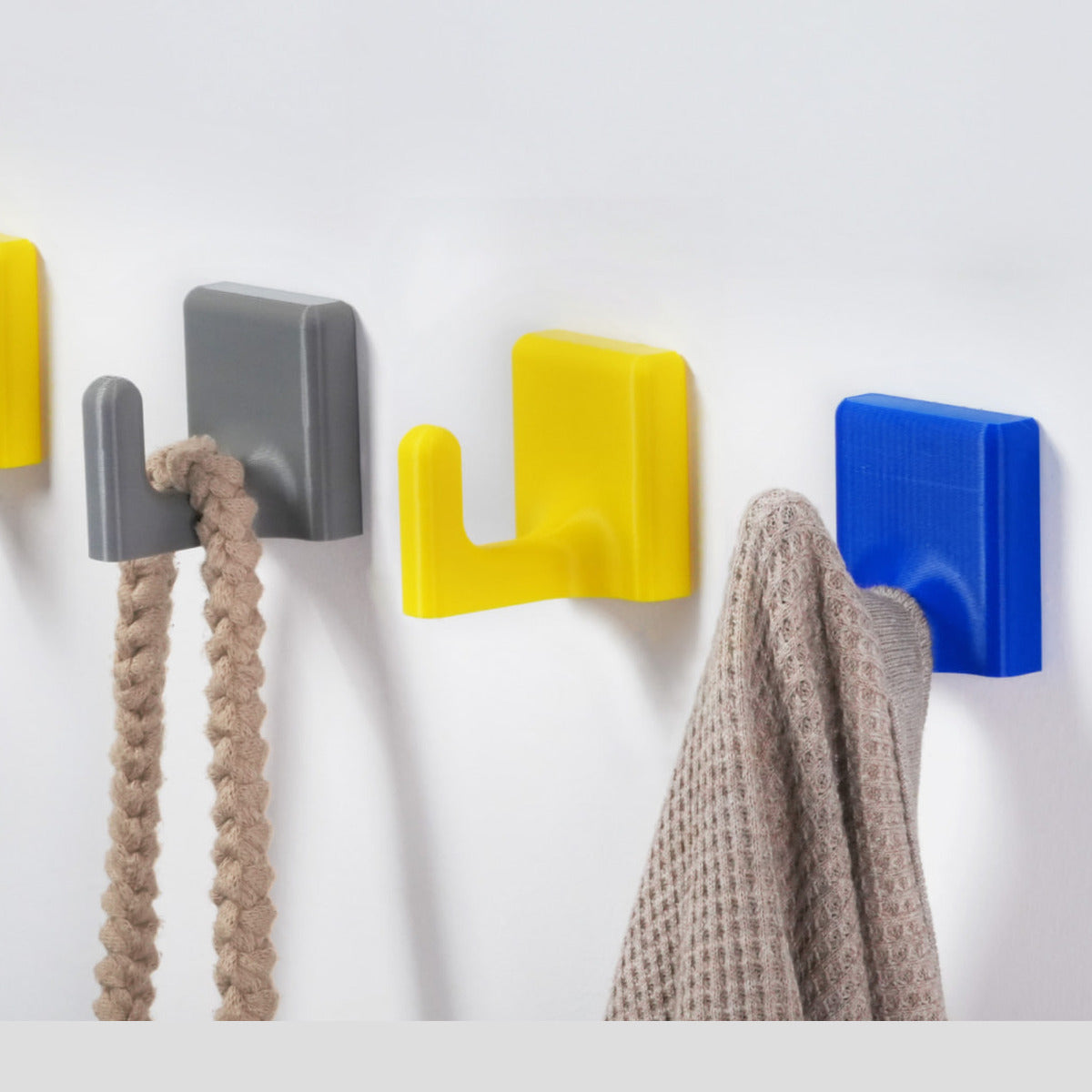 Grey/yellow/blue wall hooks holding braided strap + knit fabric (tough everyday use)