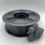 A spool of matte black 3D printer filament with a small duck-shaped sample printed from the filament, displayed on a light gray background.