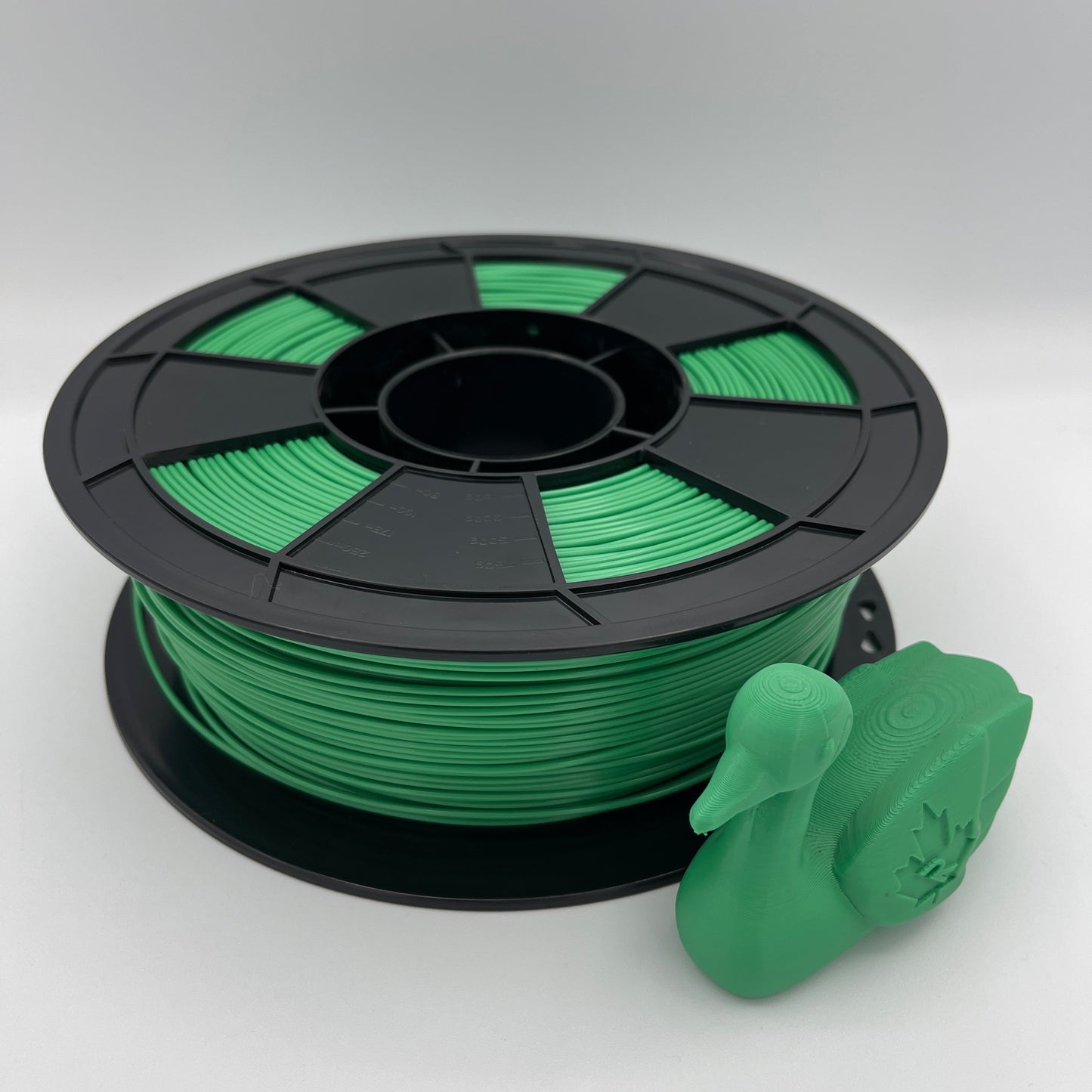 A spool of bright green 3D printer filament with a black plastic core, shown next to a small green 3D-printed duck model on a light gray background.