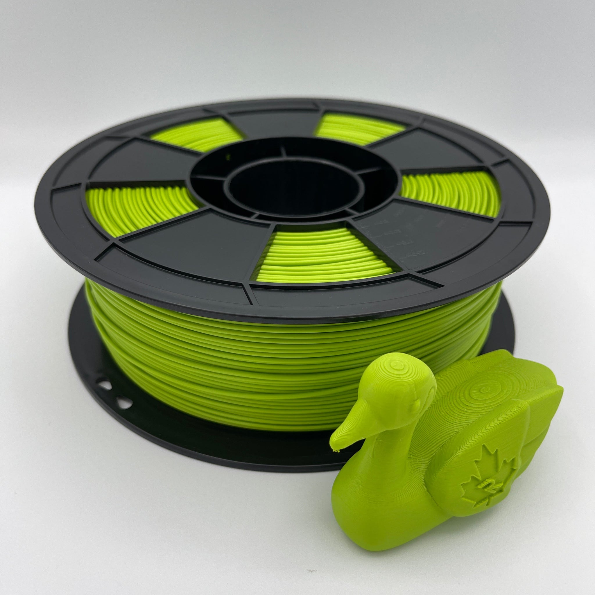 A spool of bright lime green 3D printer filament next to a small molded duck-shaped object, photographed on a clean white studio background.