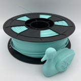 A spool of mint green 3D printer filament with a small mint green duck-shaped object placed in front, photographed on a clean light gray studio background.
