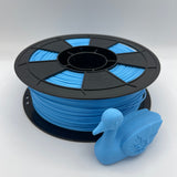 A spool of bright blue 3D printer filament with a black plastic core, shown alongside a small blue duck-shaped printed object on a light gray background.